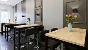Habitación de hotel moderna con un ventanal grande, una mesa de madera, sillas negras y un florero con flores.