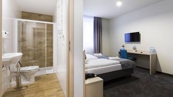 Habitació d'hotel amb dutxa, vàter, bany, llit, escriptori i televisió.