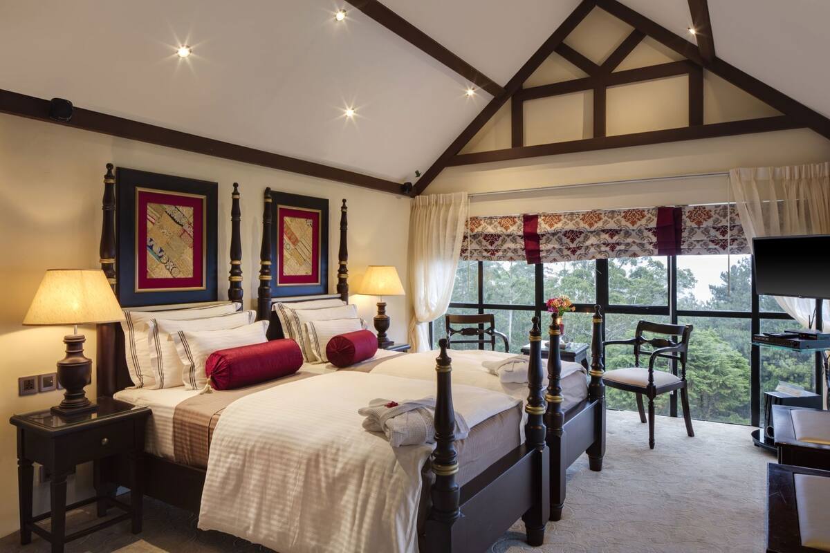 Une chambre à coucher avec un lit à baldaquin, deux tables de chevet, un bureau avec une chaise et une grande fenêtre donnant sur un beau paysage.