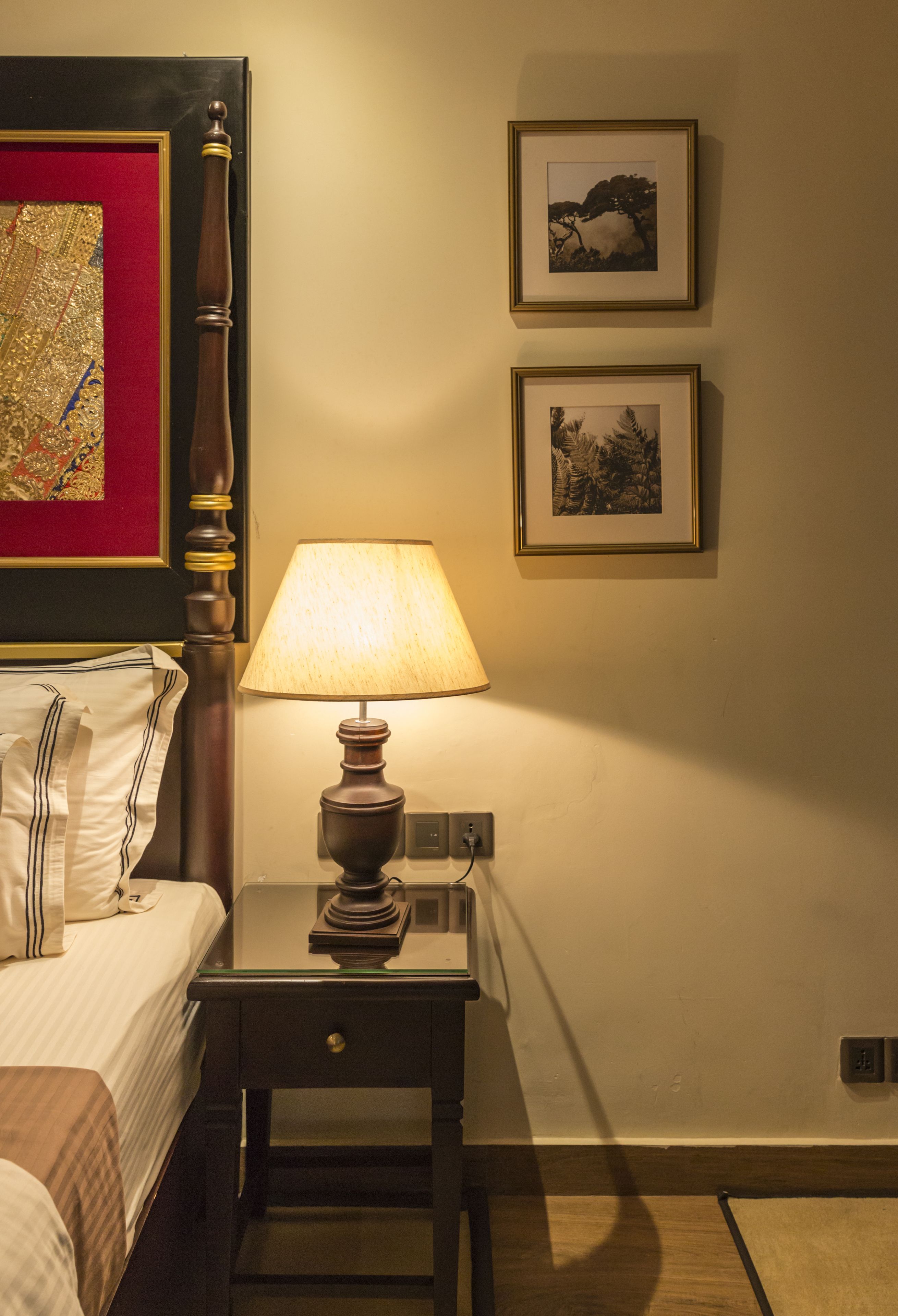 A hotel room with a bed, a nightstand with a lamp, and two framed pictures on the wall.