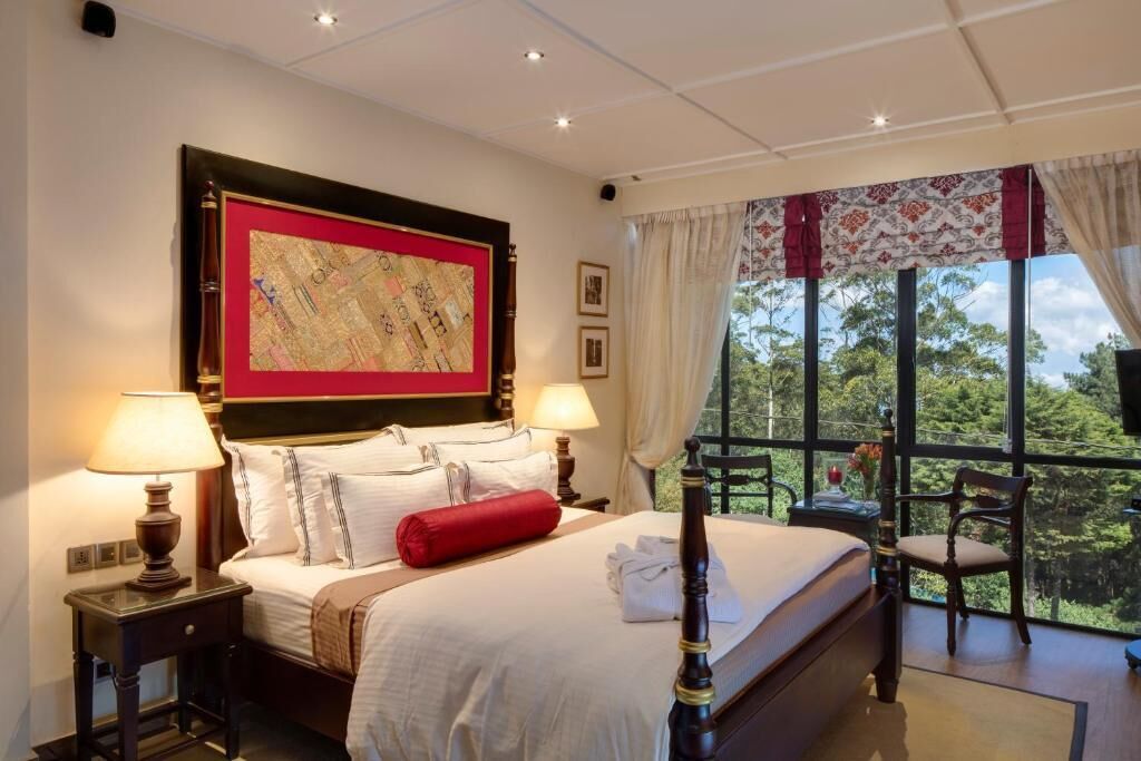 A hotel room with a large bed, two bedside tables with lamps, a map on the wall, a window with curtains, and a view of greenery outside.