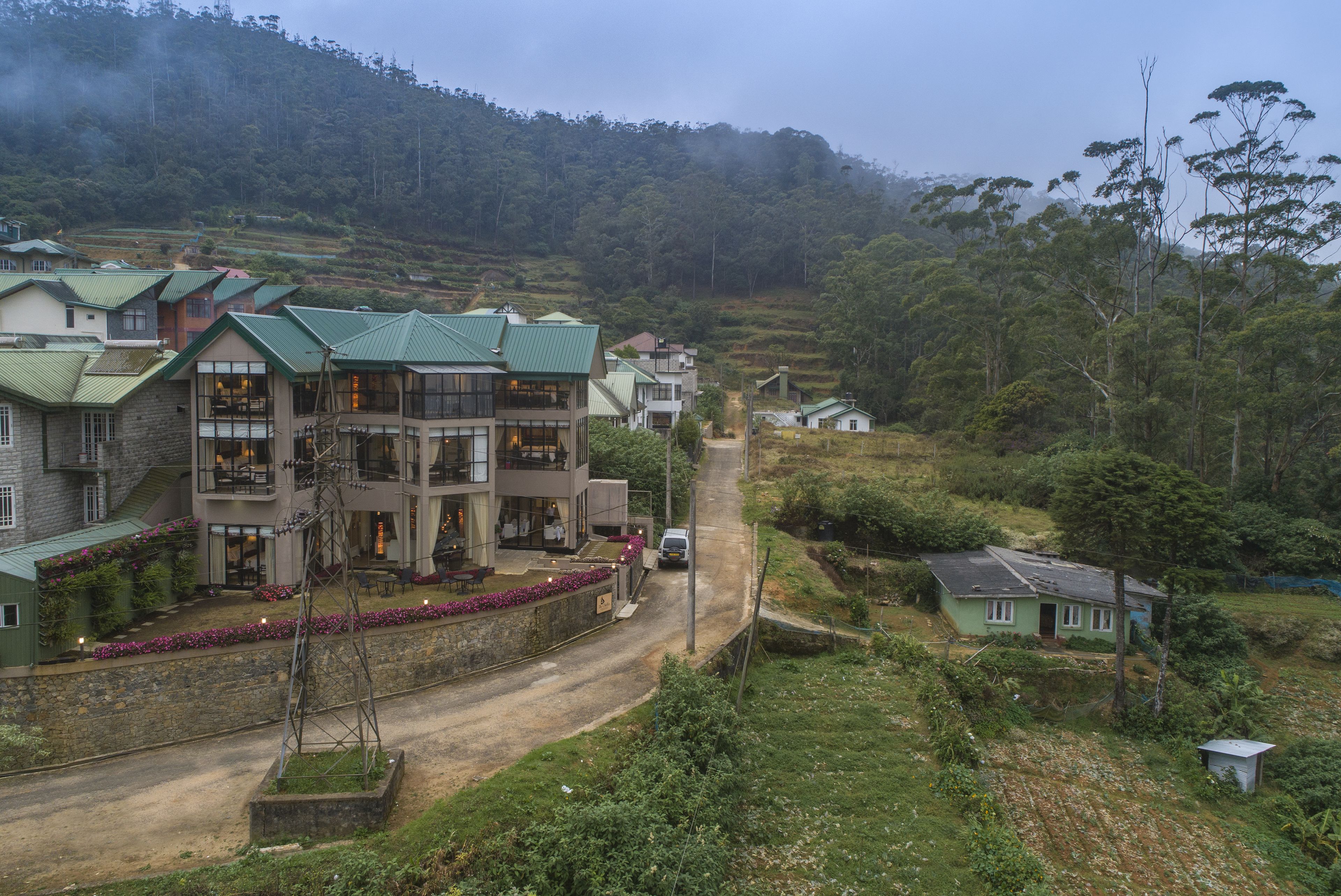 Un quartier résidentiel situé sur une colline, avec de nombreuses maisons, un chemin de terre et une végétation luxuriante.