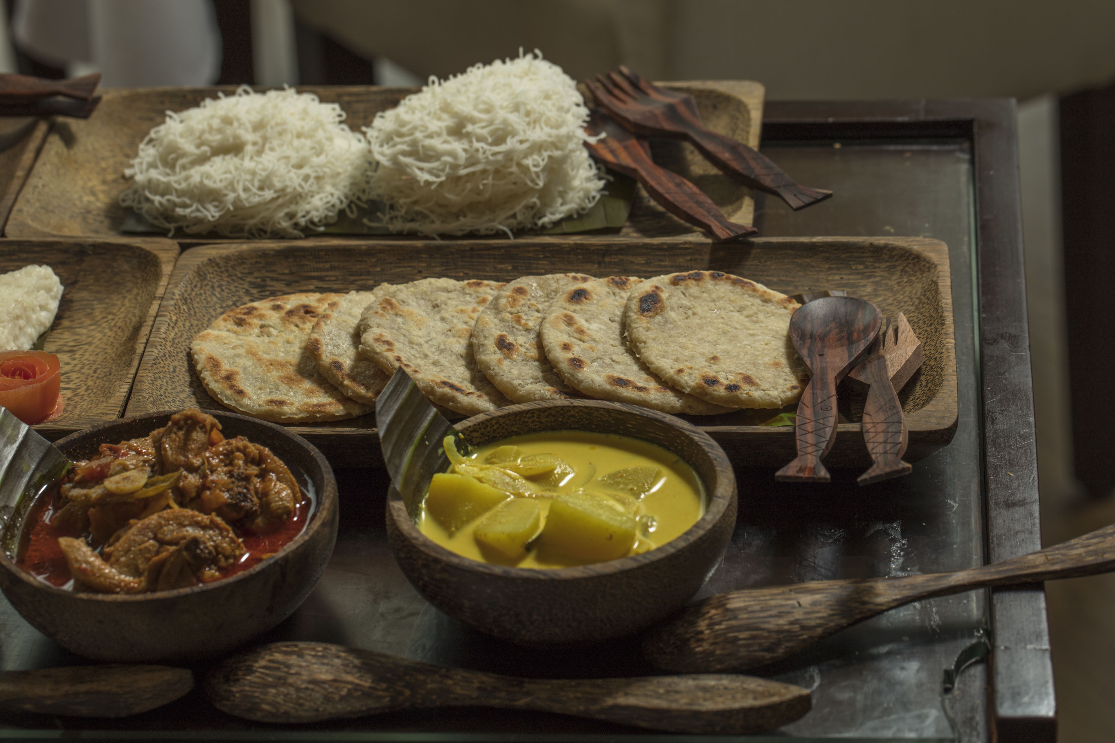 A wooden table with various dishes including rice, flatbreads, a curry, and a bowl of stew.