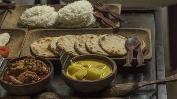 A wooden table with various dishes including rice, flatbreads, a curry, and a bowl of stew.