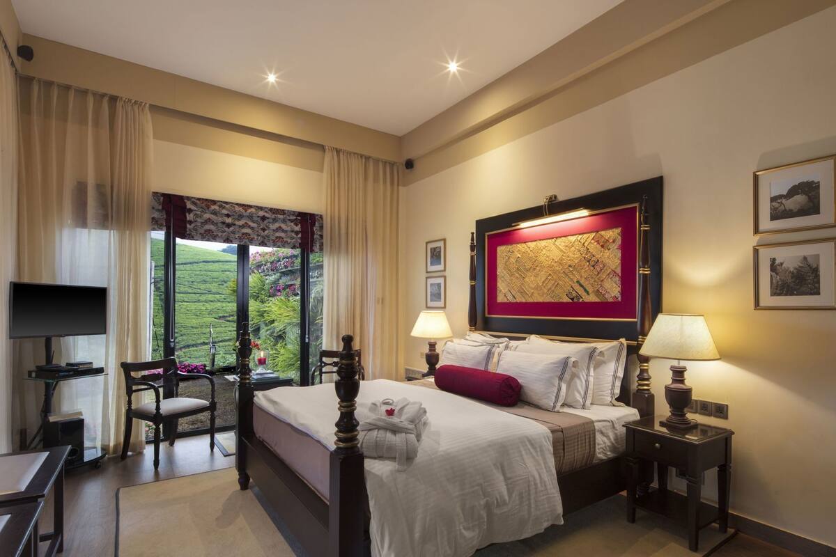 Une chambre d’hôtel comprenant un lit, des tables de chevet, un bureau, une chaise et une grande fenêtre donnant sur un beau paysage.