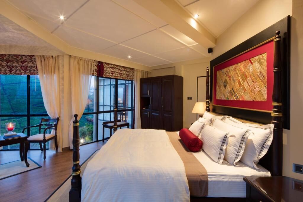 Quarto de hotel com uma cama grande, uma escrivaninha com cadeira, uma janela com cortinas e um quadro na parede.