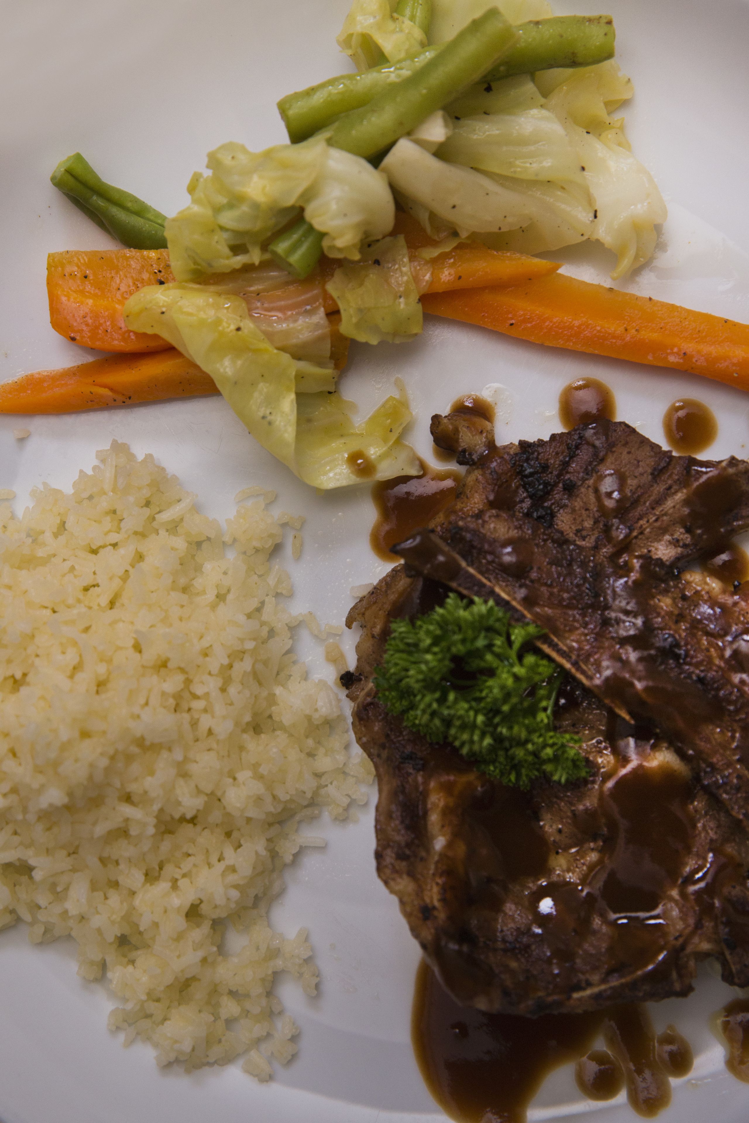 A plate with a beef steak, rice, and mixed vegetables including carrots and green beans.
