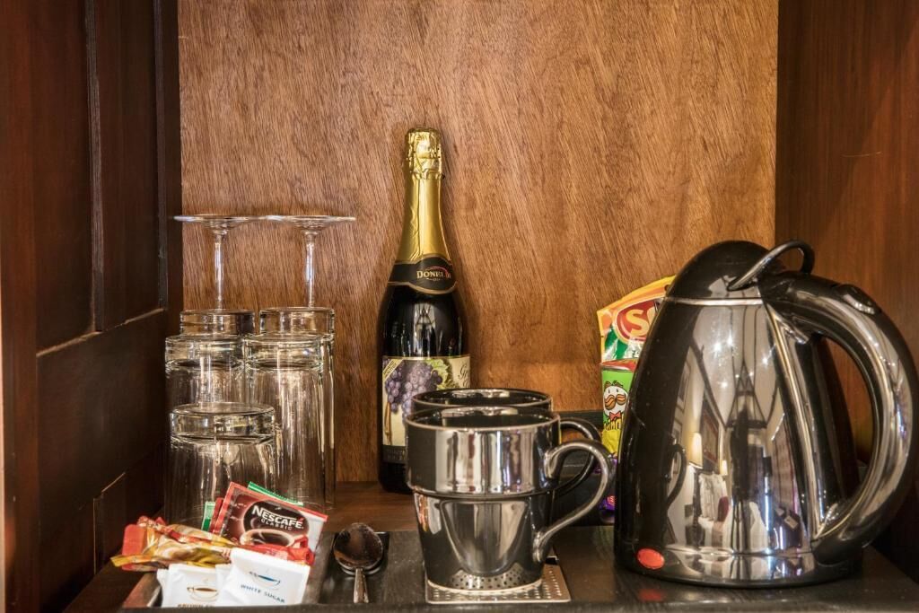 A minibar setup with a bottle of champagne, multiple glasses, a coffee maker, and some coffee pods.