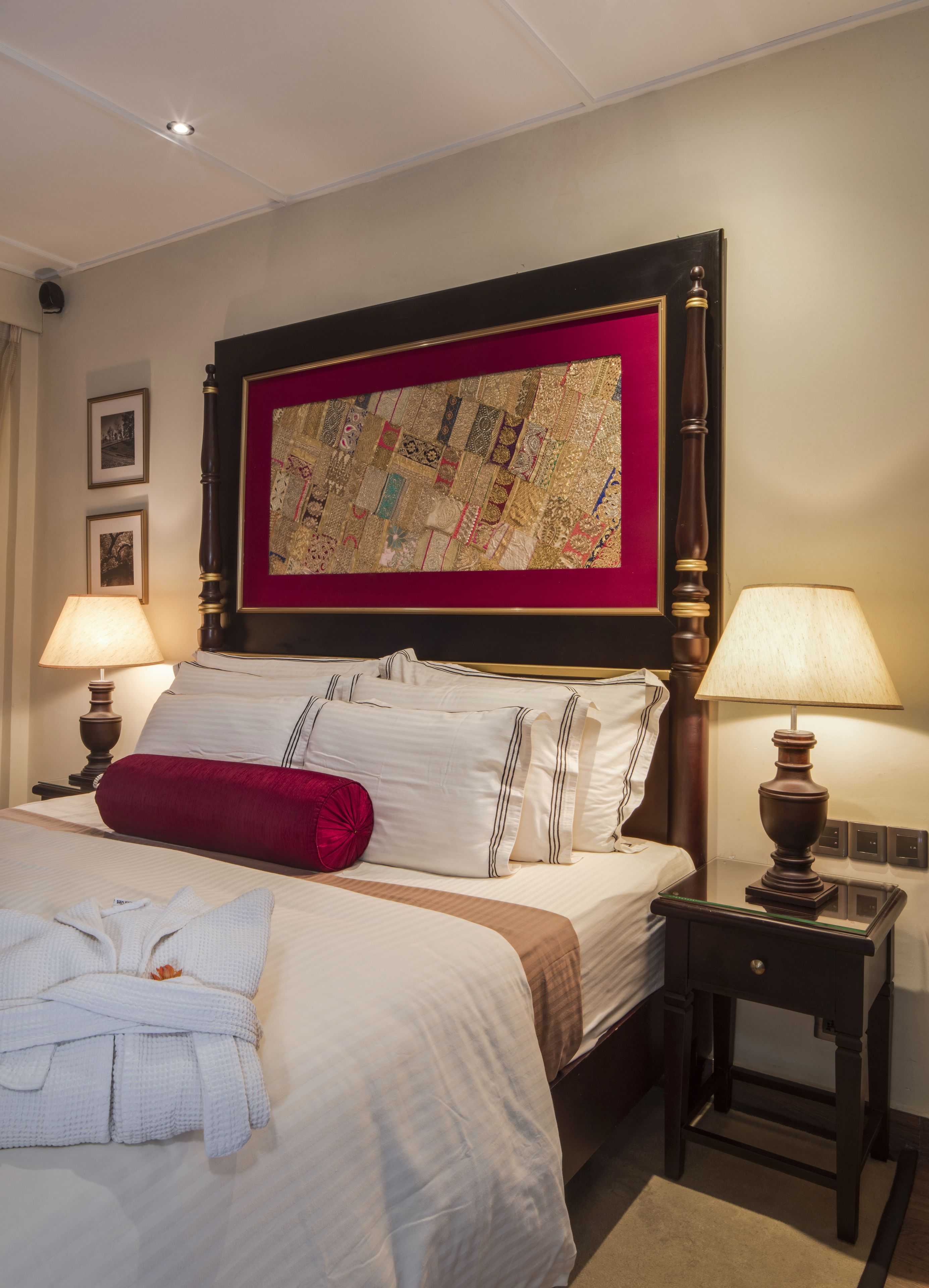 A hotel room with a large bed, two bedside lamps, a quilt, and a framed artwork above the bed.