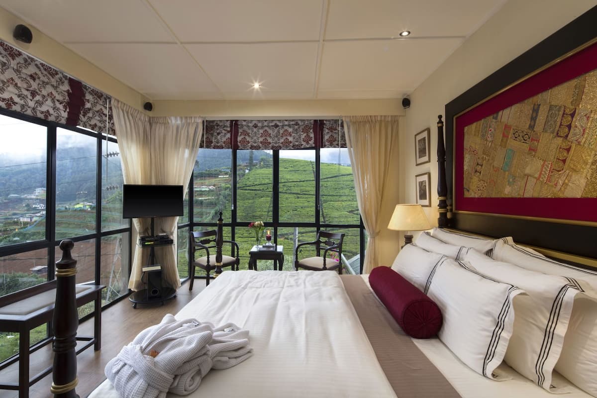 Une chambre d’hôtel avec un grand lit, une télévision, un bureau avec une lampe et une vue sur un paysage verdoyant.
