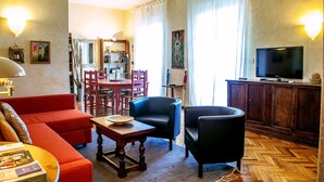 Un salon avec un canapé rouge, un fauteuil noir, une table basse en bois, une table à manger avec des chaises et un téléviseur posé sur un meuble en bois.