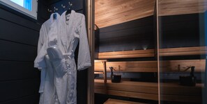 A sauna room with wooden benches and a white robe hanging on a rack.