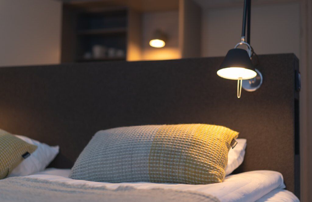 Ein ordentlich bezogenes Bett mit einem gemusterten Kopfkissen und einer Nachttischlampe.