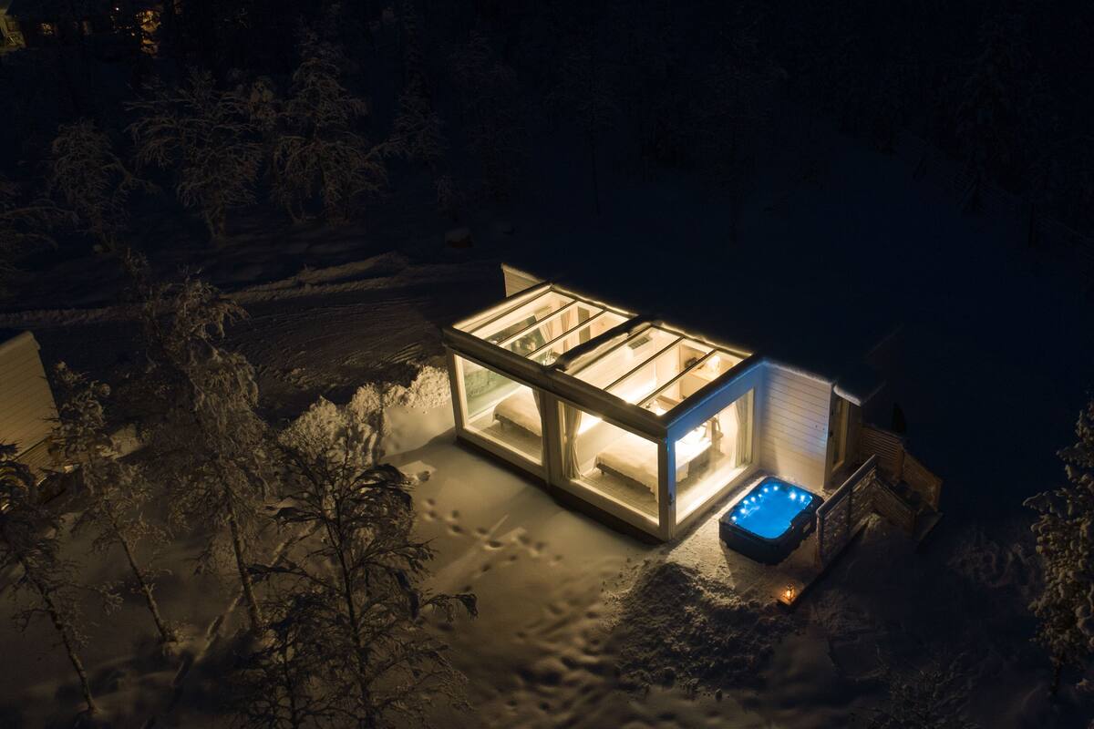 Moderni lasitalo, jossa on poreallas, lumisen maiseman keskellä yöllä.
