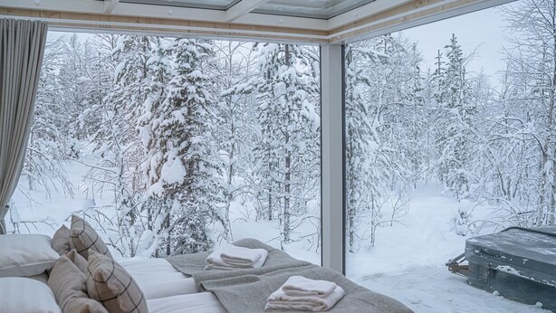 Ein Zimmer mit großem Fenster mit Blick auf einen verschneiten Wald.