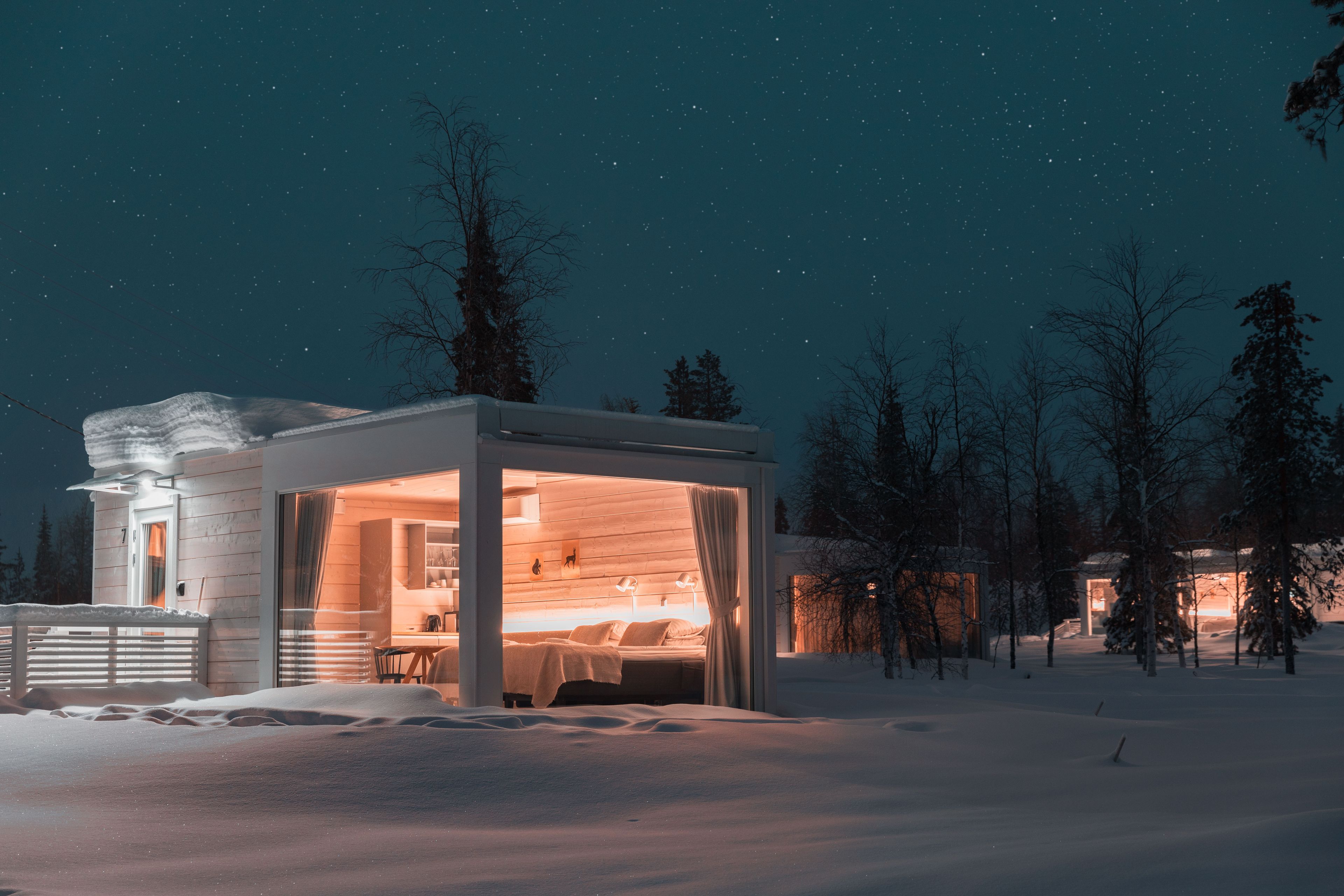 Ein modernes, schneebedecktes Blockhaus mit Glastür, einem sichtbaren Bett und einem Essbereich.