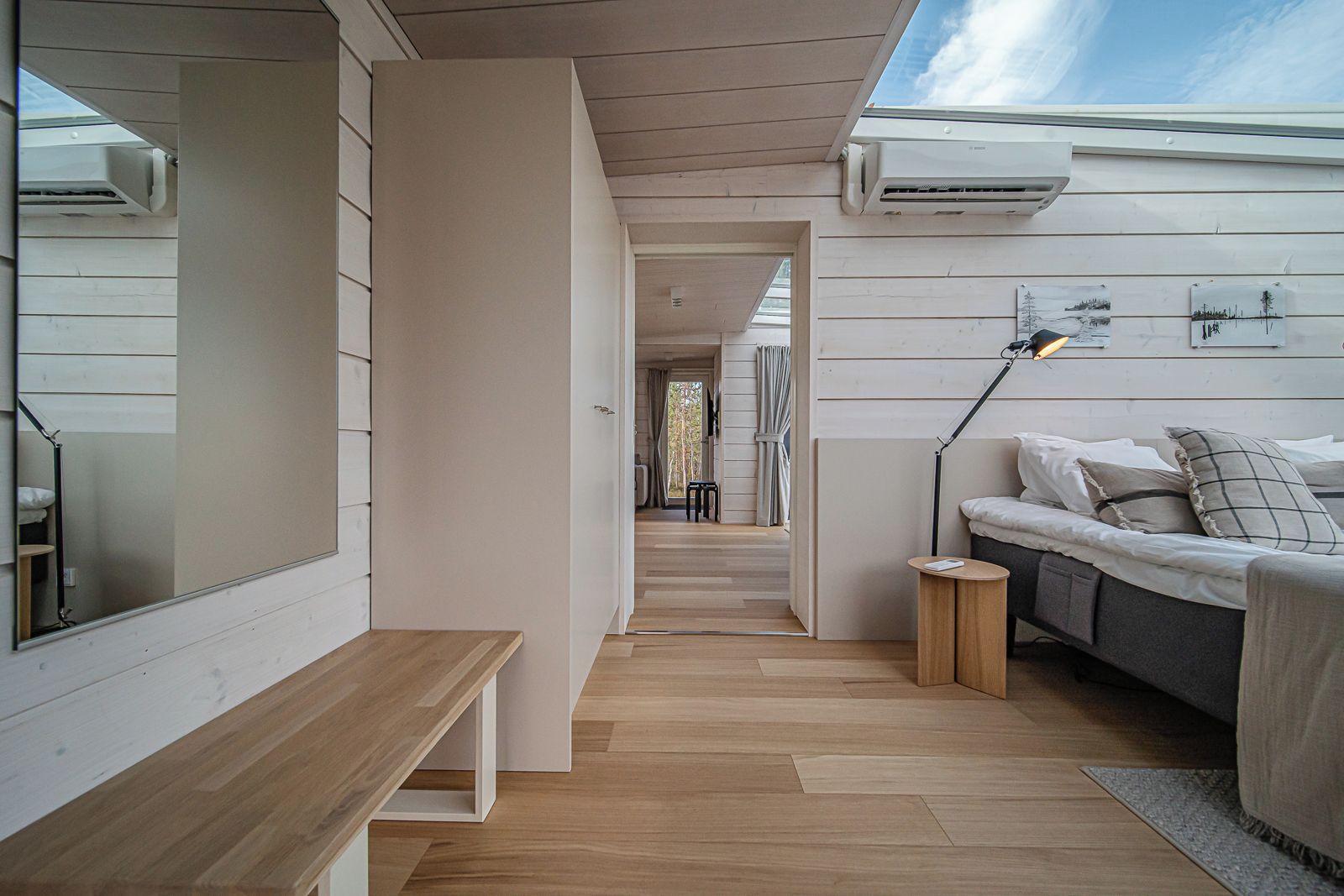 A modern interior with a wooden bench, a sofa, and a desk. There are air conditioning units on the wall and a view of the outdoors.