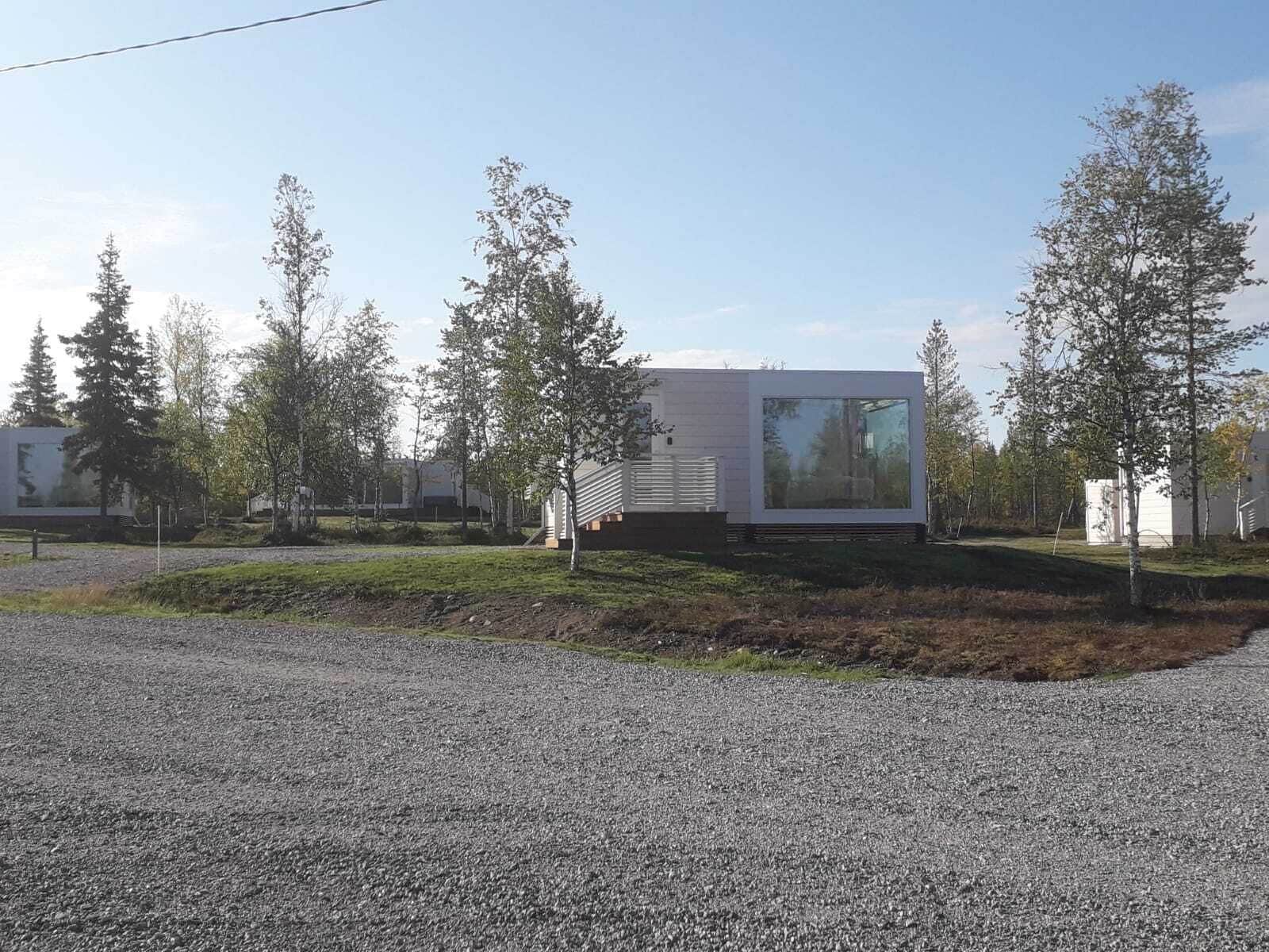 A modern building with a large glass window, surrounded by trees and a gravel driveway.