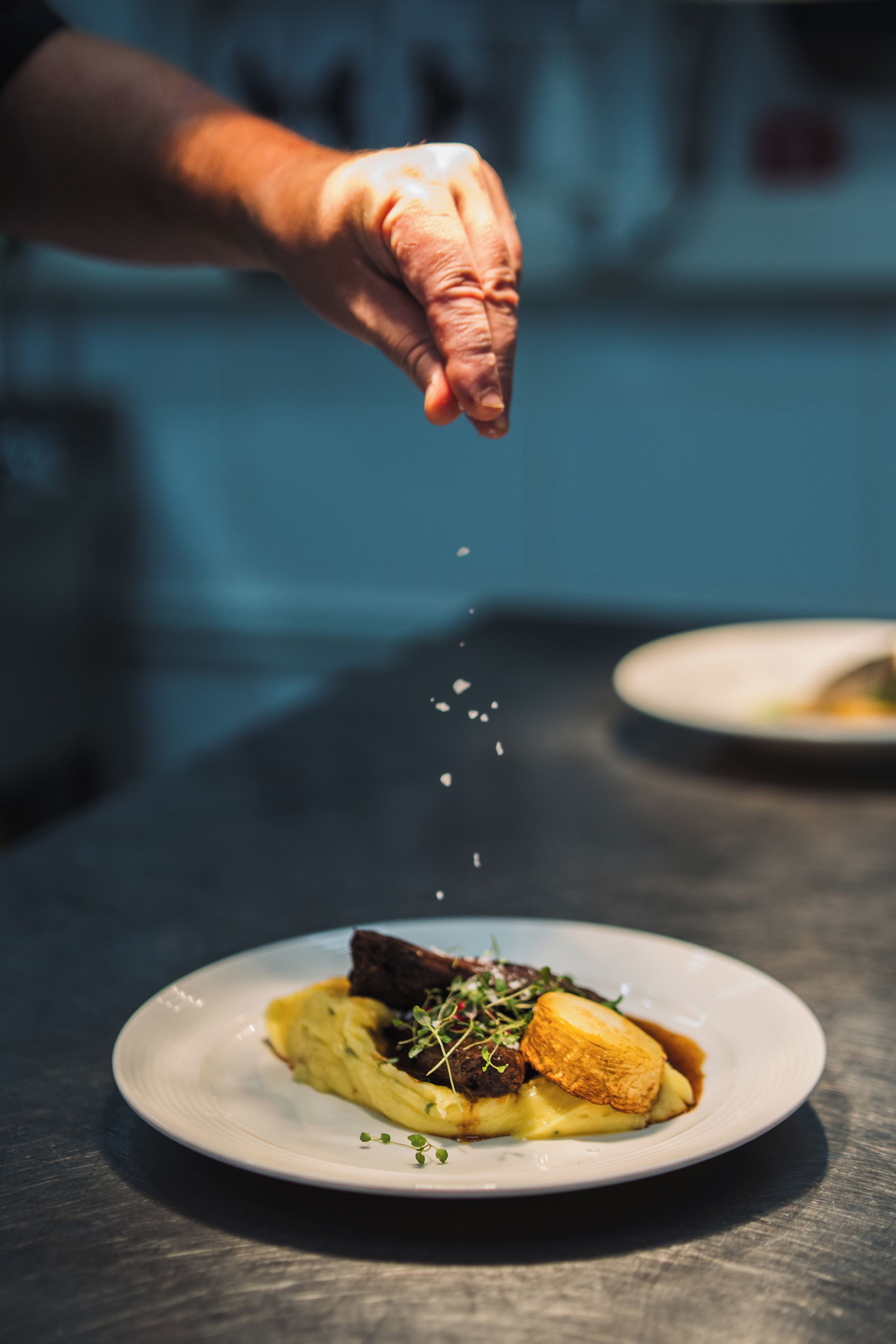 A hand sprinkling seasoning over a dish on a plate.