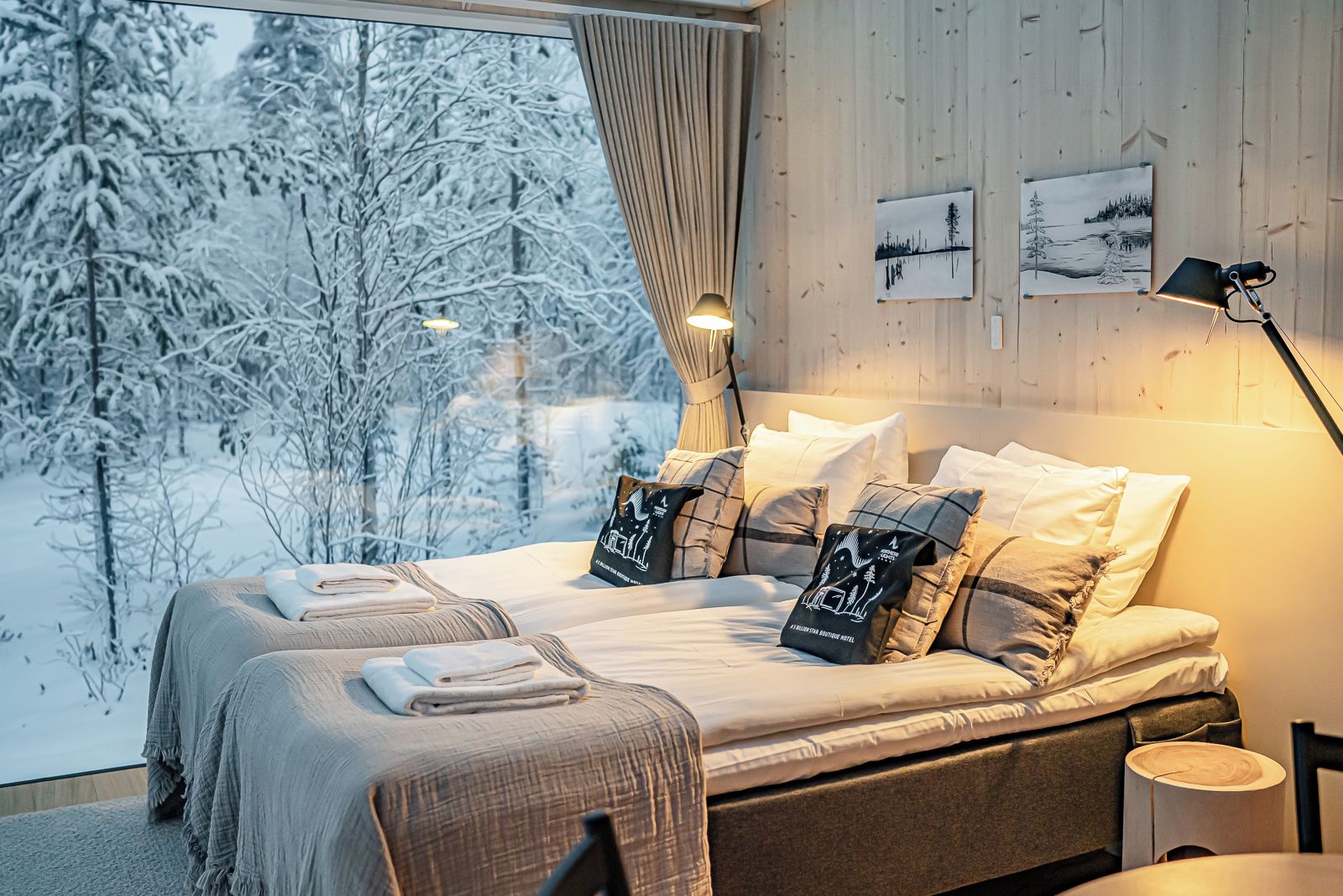 A bedroom with a large window, a bed with multiple pillows, a bedside table, and a lamp.