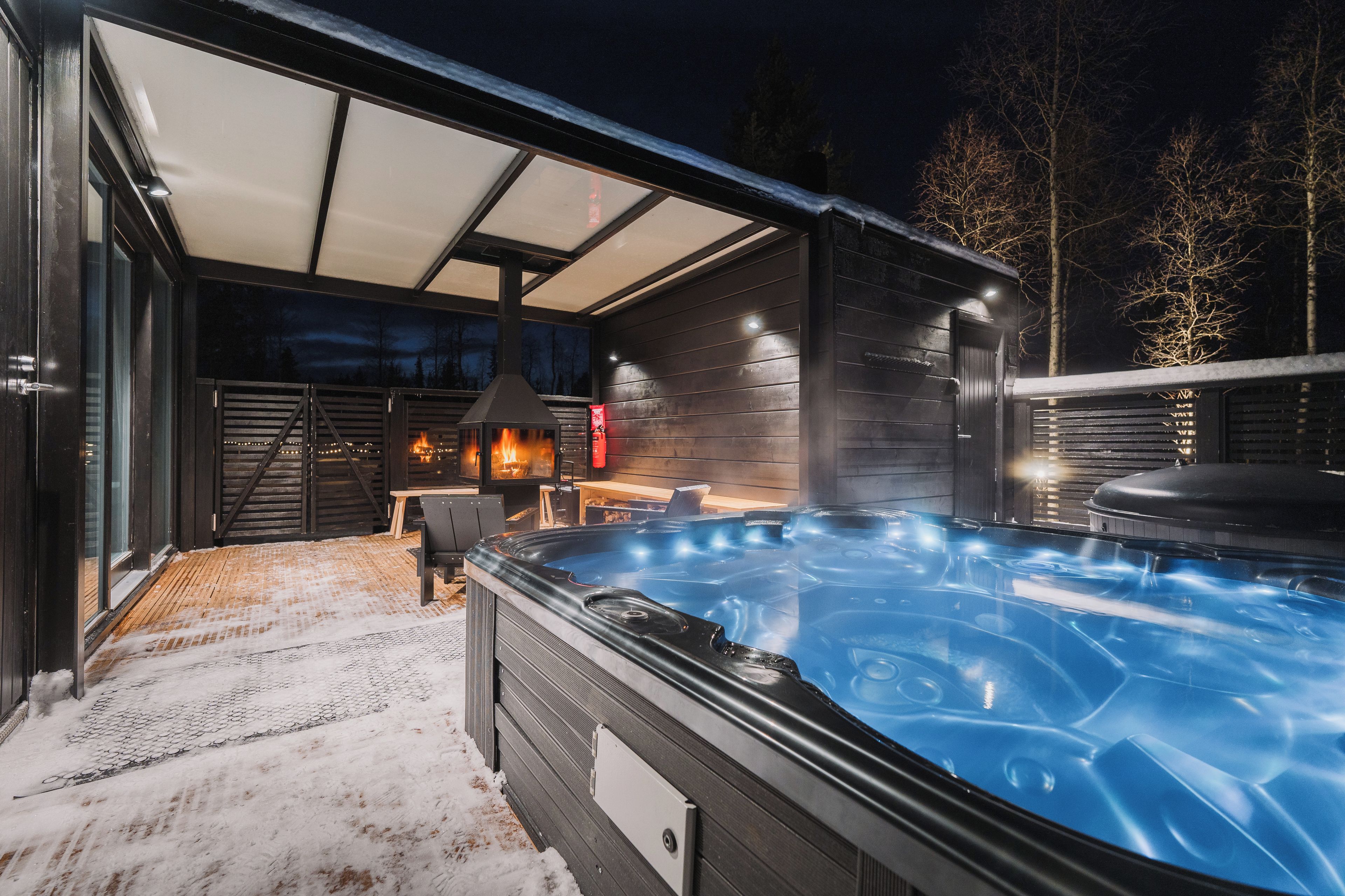 A hot tub with a wooden deck and a covered seating area with a fire feature.