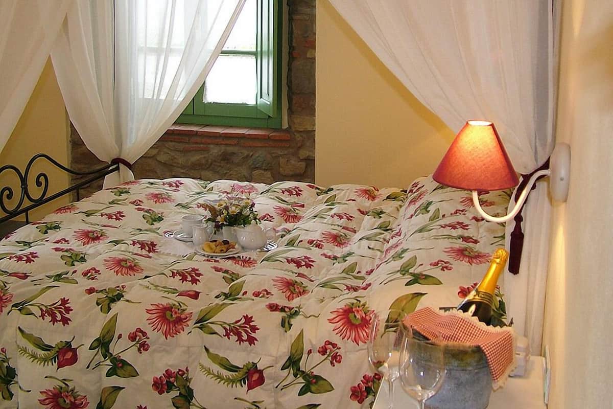 A bedroom with a floral bedspread, a bedside table with a lamp, and a window with curtains.