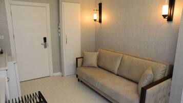 Une pièce avec un canapé beige, une porte blanche et un luminaire fixé au mur.