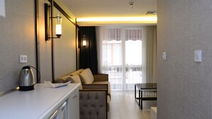A modern hotel room with a sofa, a small table, and a kettle on the counter. - Gardenya Suit Hotel (Trabzon)