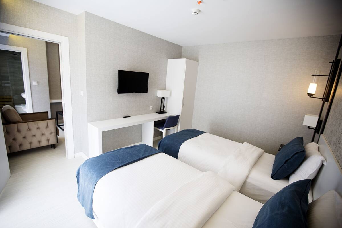 A hotel room with two beds, a desk, a chair, a television, and a lamp.