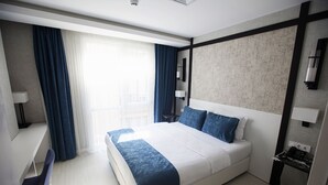 A modern hotel room with a large bed, a desk, and a view of the city. - Gardenya Suit Hotel (Trabzon)