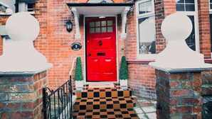 Una puerta roja con un alero blanco y un escalón a cuadros blanco y negro que la precede.