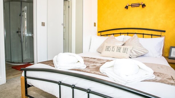 Una habitación de hotel con cama, cabina de ducha de vidrio y una pared de acento amarilla.