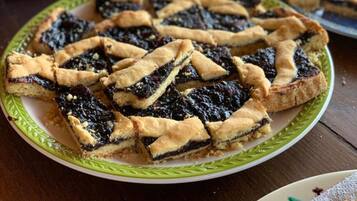 A plate of fruit tarts with a lattice crust, a cake in the background, and a basket of breadsticks.