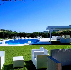 A swimming pool with white lounge chairs and a covered area, surrounded by a well-maintained lawn and trees. - Agriturismo Trappeto Vecchio (San Demetrio Corone)