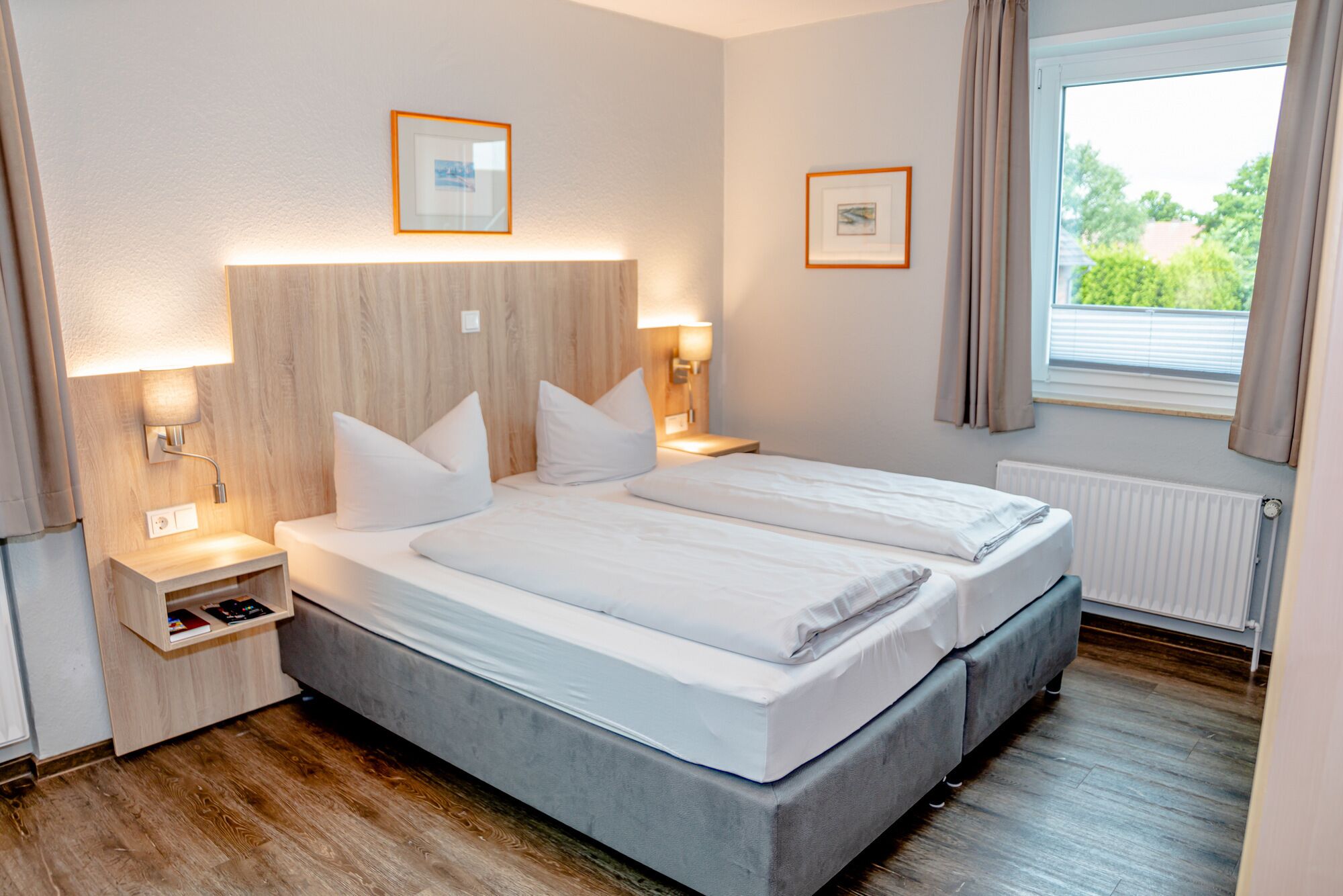 Una camera d'albergo moderna con un letto matrimoniale, comodini, lampade a parete e quadri incorniciati.