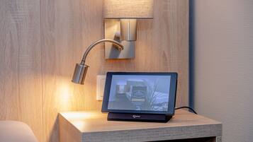 Een tablet op een houten nachtkastje, met een wandlamp en een stopcontact.