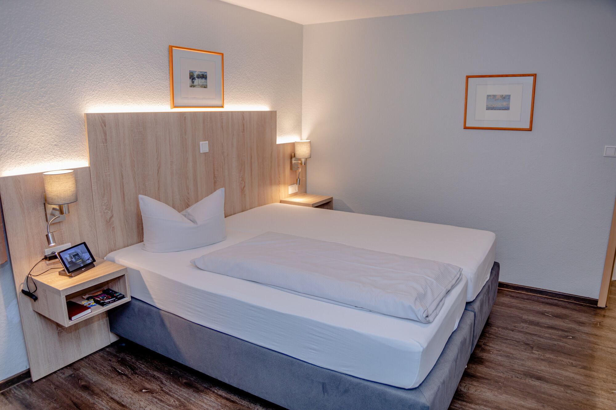 A modern hotel room with a large bed, bedside tables, and wall-mounted lamps.