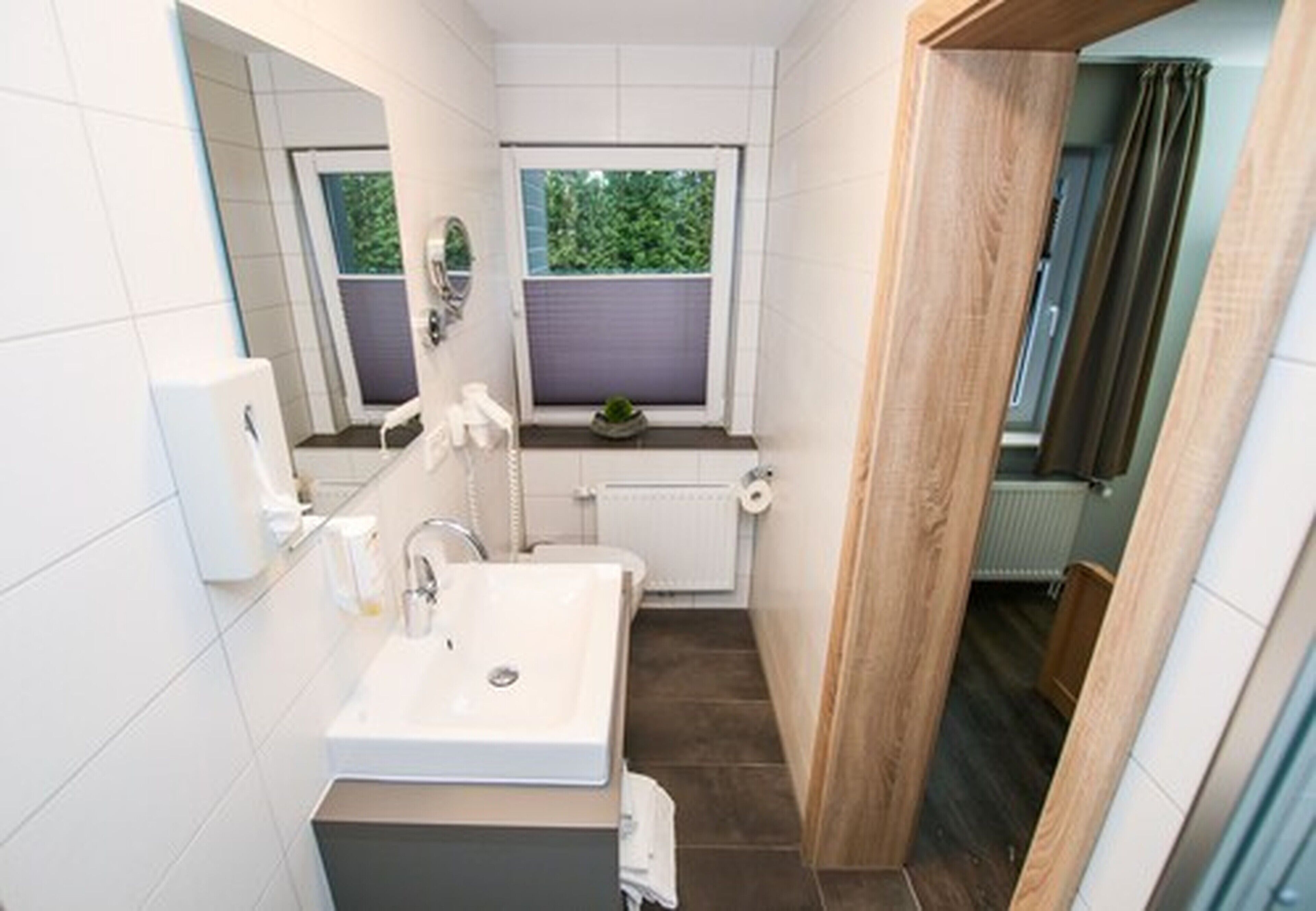 Un baño pequeño con lavamanos, espejo y ventana blancos.