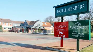Un letrero de hotel con 'HOTEL HERBERS' y un letrero rojo del 'Restaurante Löwen' con el logotipo de un cerdo.