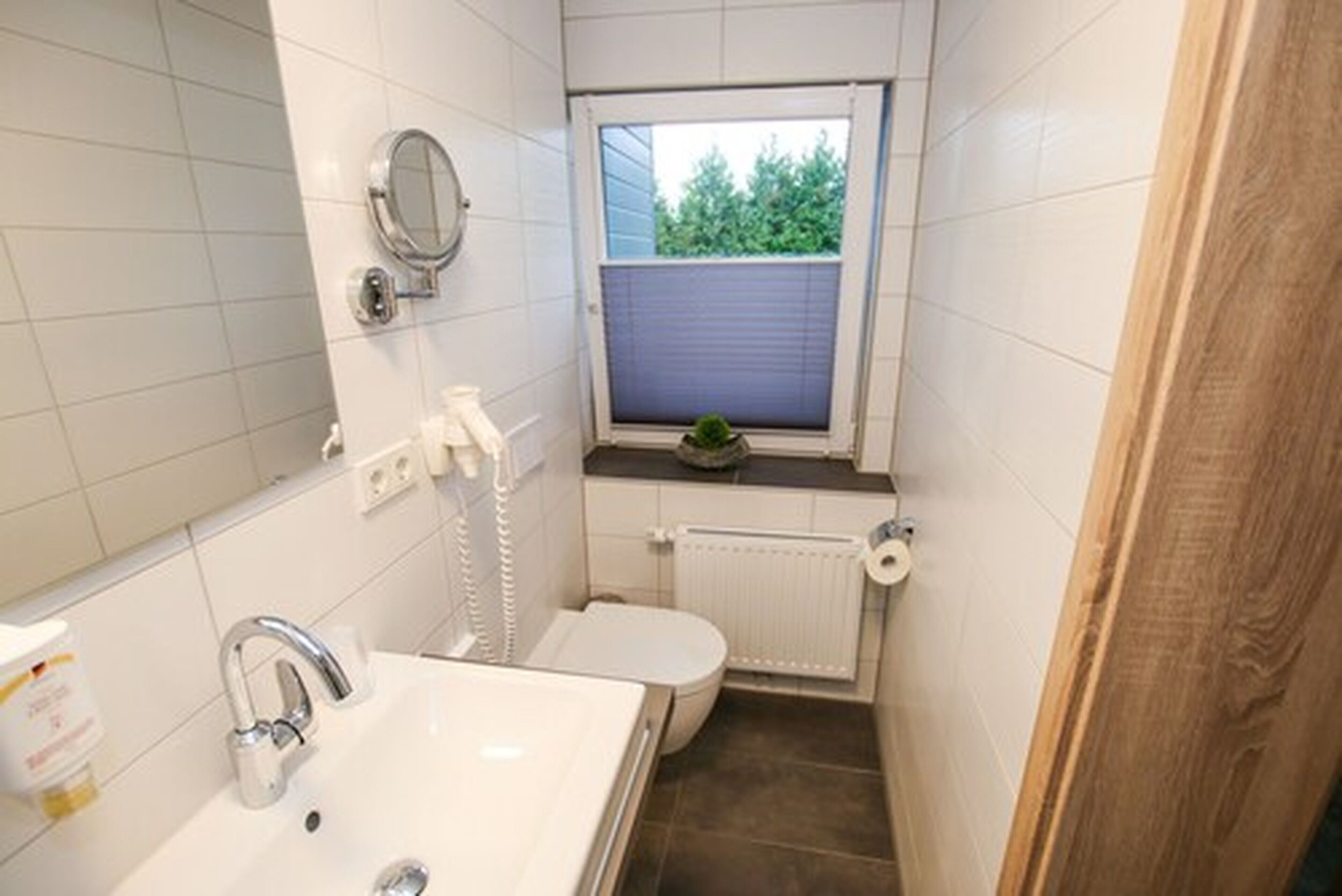 Et lille, kompakt badeværelse med en hvid vask, toilet og et vindue over toilettet.