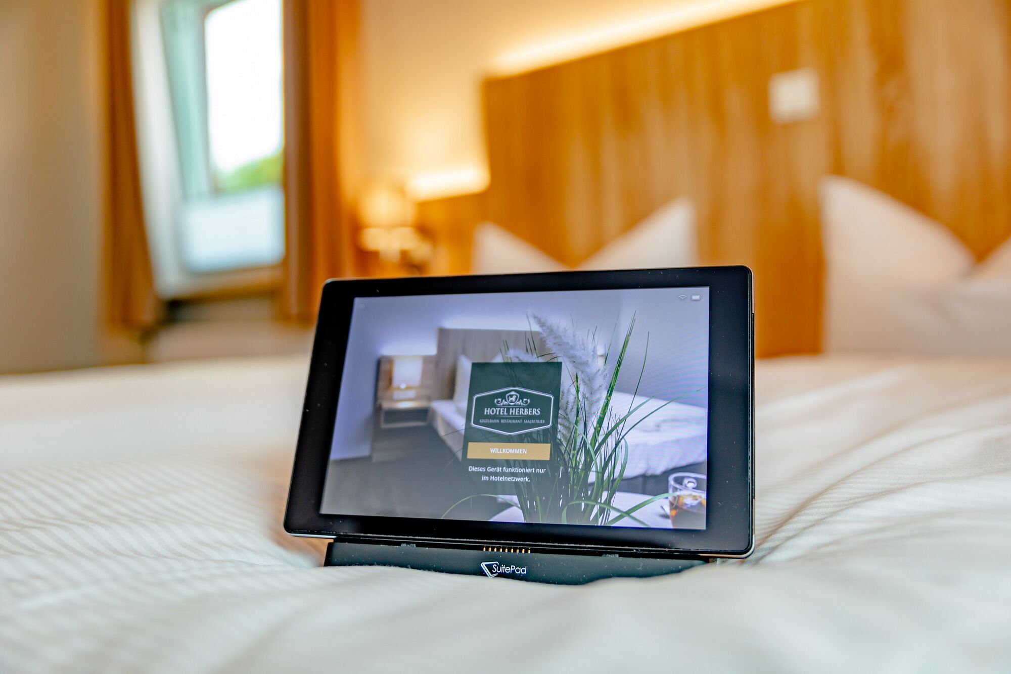 A tablet displaying a hotel room with a bed, pillows, and a bedside table.