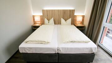 Una cama doble con cabecera de madera, dos mesitas de noche con lámparas y una ventana con cortinas.