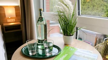 Una habitación con una mesa redonda, una botella de agua, dos vasos, una planta en maceta y un folleto.
