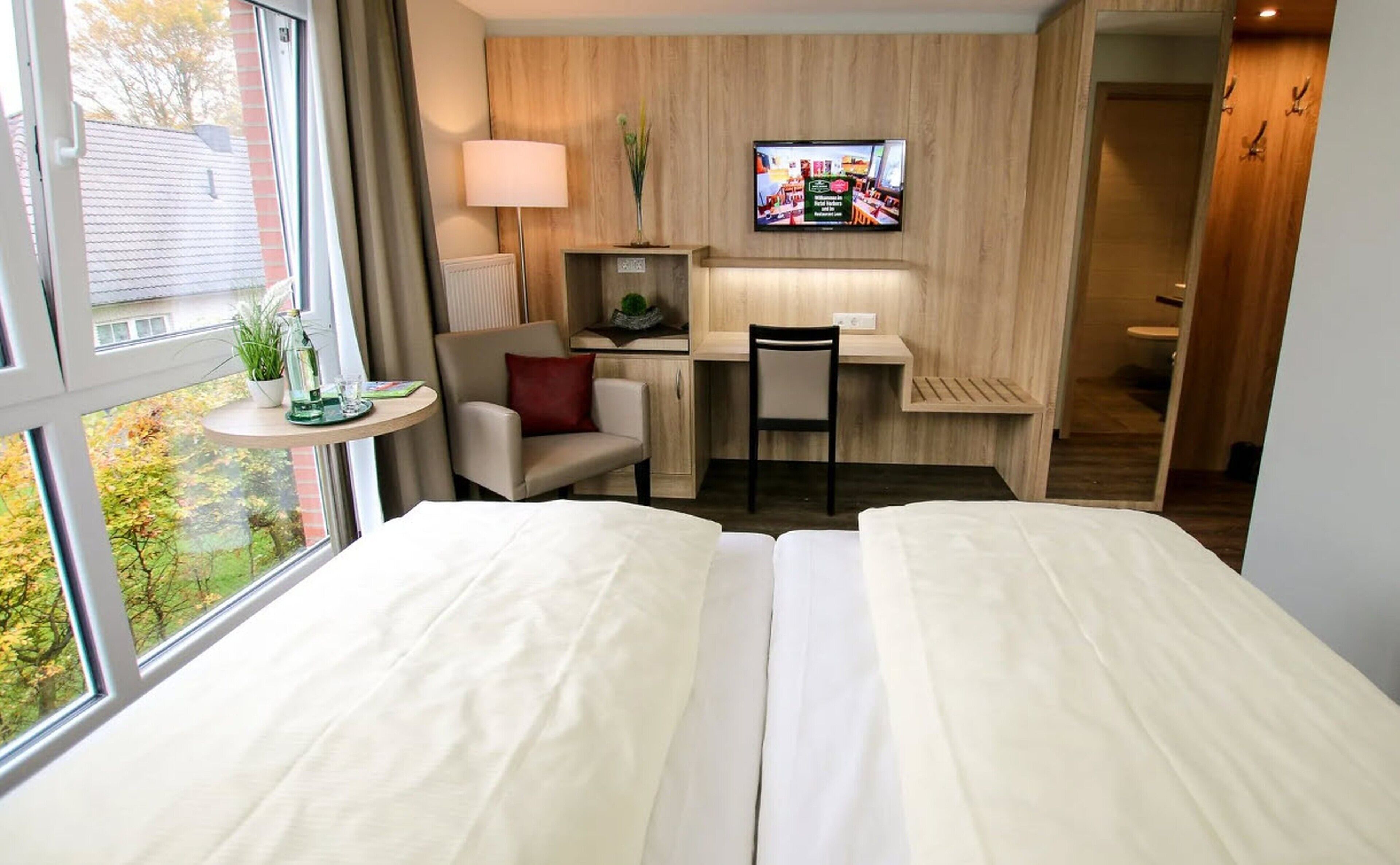 Ein Hotelzimmer mit Bett, Schreibtisch, Stuhl, Fernseher und Fenster mit Blick auf Bäume.