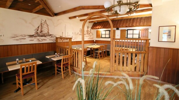A restaurant with wooden furniture, a high ceiling, and a mural of a sailboat. - Hotel Herbers & RestaurantLeon (Sudbrookmerland)