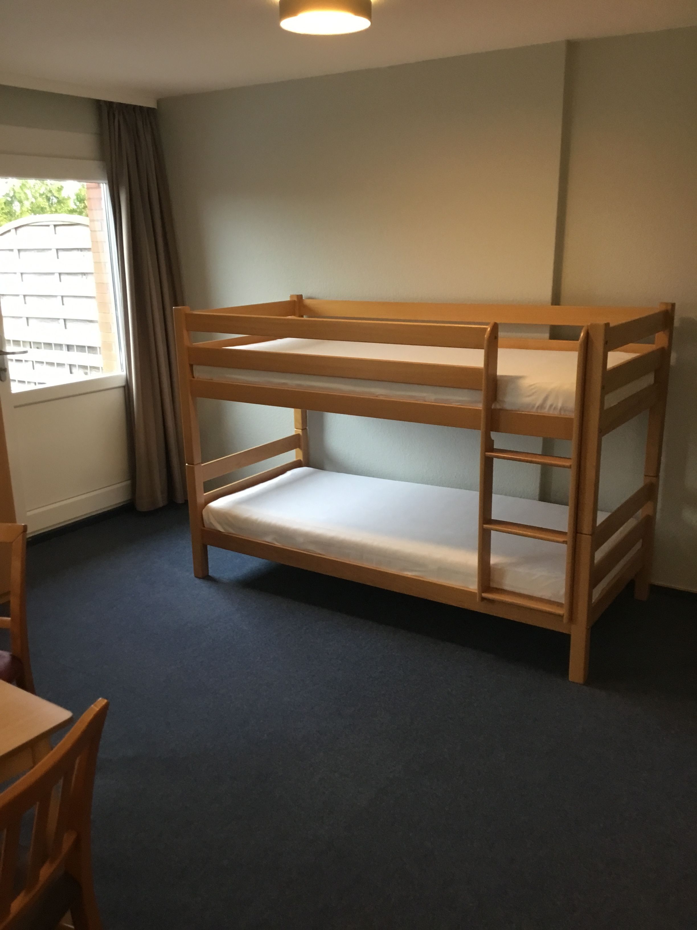 A bunk bed in a room with a window, a desk, and a chair.