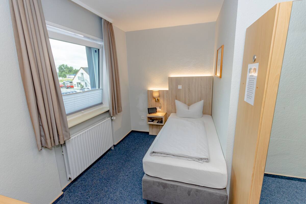 Een hotelkamer met een bed, nachtkastje, lamp, raam met gordijnen en uitzicht.