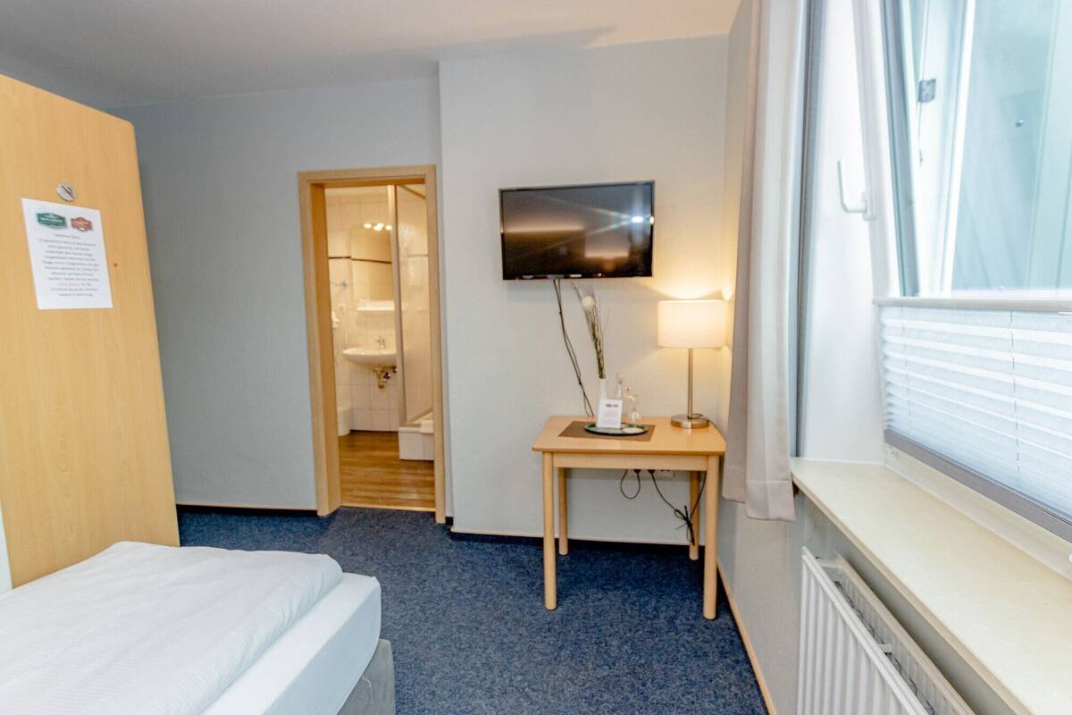Een hotelkamer met een bed, een televisie, een bureau met lamp, een badkamer en een raam.
