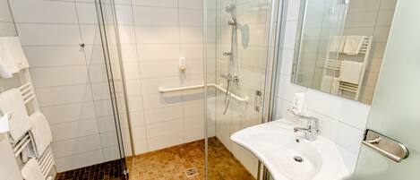 A modern bathroom with a glass shower enclosure, a white sink, and a mirror.