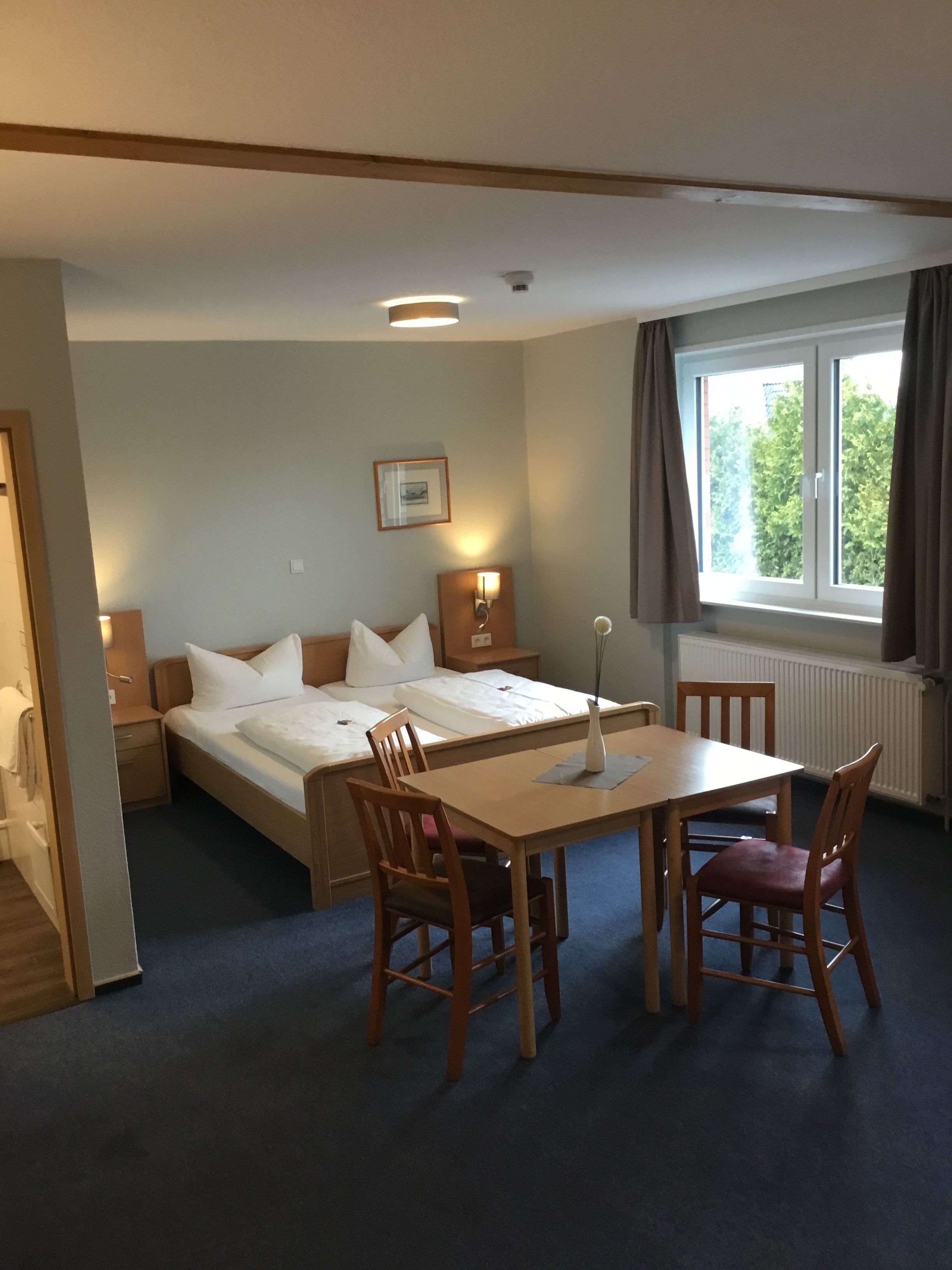 A hotel room with a bed, a desk, two chairs, a picture on the wall, and a window with curtains.